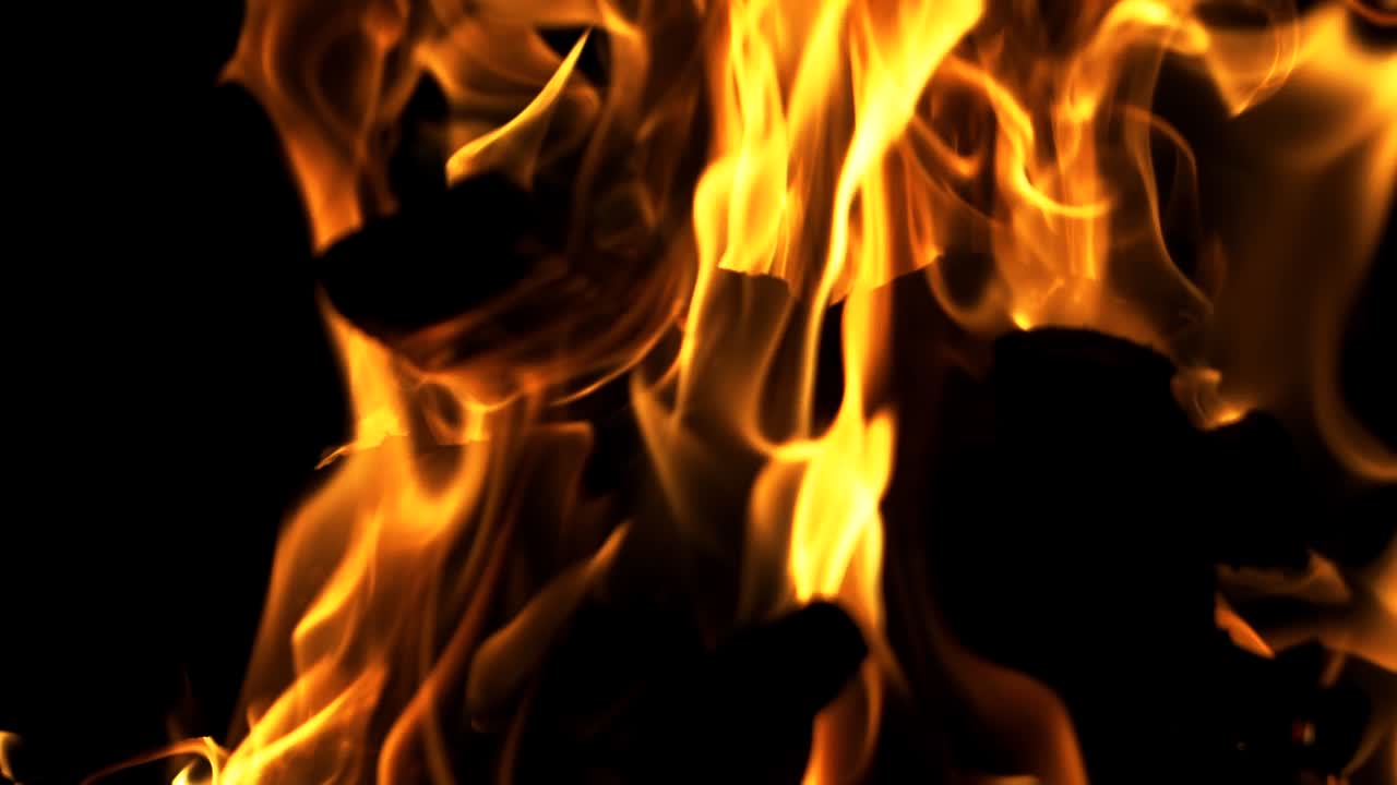 Black logs inside the bright flame burning at night on the dark background. Red flame surging up. Close-up