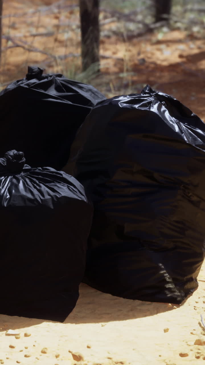 Bags of waste sit abandoned on the dry land under the scorching sun