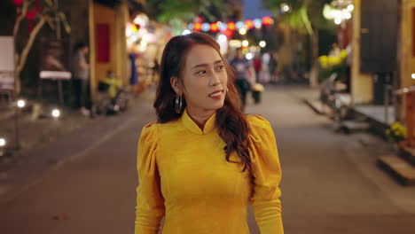 Slow-motion-follow-shot-of-attractive-Vietnamese-woman-in-traditional-clothing-walking-in-street-in-Hoi-An,-Vietnam