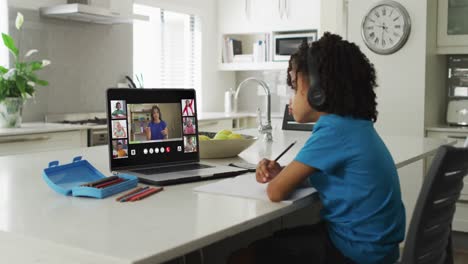 niño afroamericano usando una computadora portátil para una llamada de video con una maestra y una clase en la pantalla