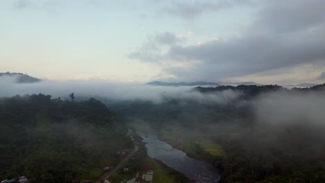 aerial dolly over misty clouds above tropical river valley gorge and homes