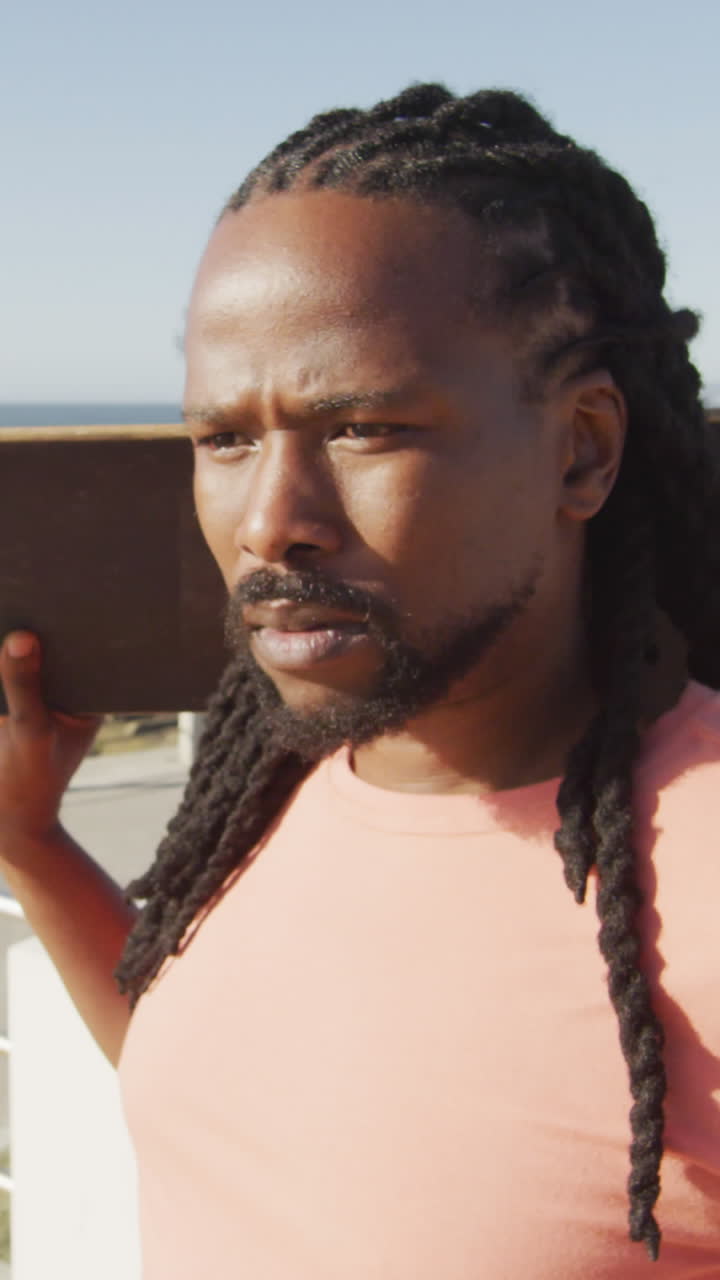 видео афроамериканца, держащего скейтборд у моря