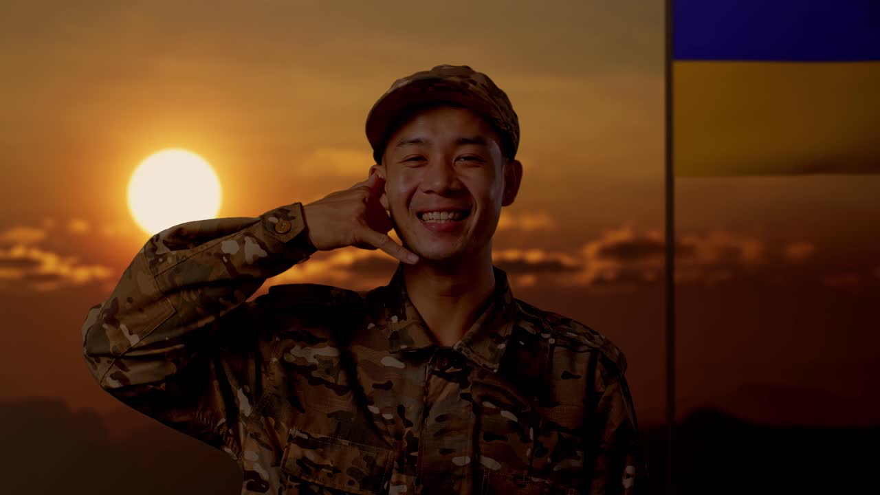 해가 지는 동안 우크라이나 국기 앞에서 전화 제스처를 하는 군인