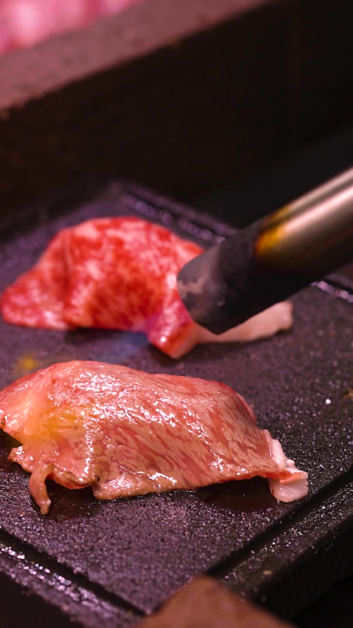 石の上でキッチンバーナーを使って炙られるプレミアムな霜降り牛肉の縦長のショット。