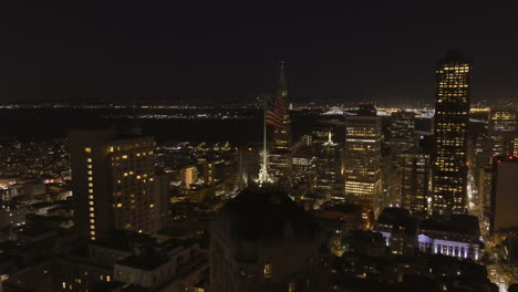 una bandiera degli stati uniti che sventola di notte su un edificio alto con lo skyline della città di san francisco come sfondo - parallasse aerea modificata alla fine per una transizione