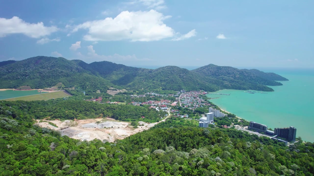 Filmatisk droneopptak av Penang, Malaysia, som viser et tropisk kystsamfunn omgitt av grønne fjell, turkist hav og et ferskvannsreservoar adskilt av landskapet