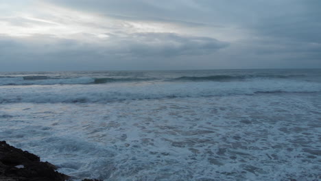 epic drone shot gliding past a man standing on a cliff's edge while ferocious waves crash onto the shore