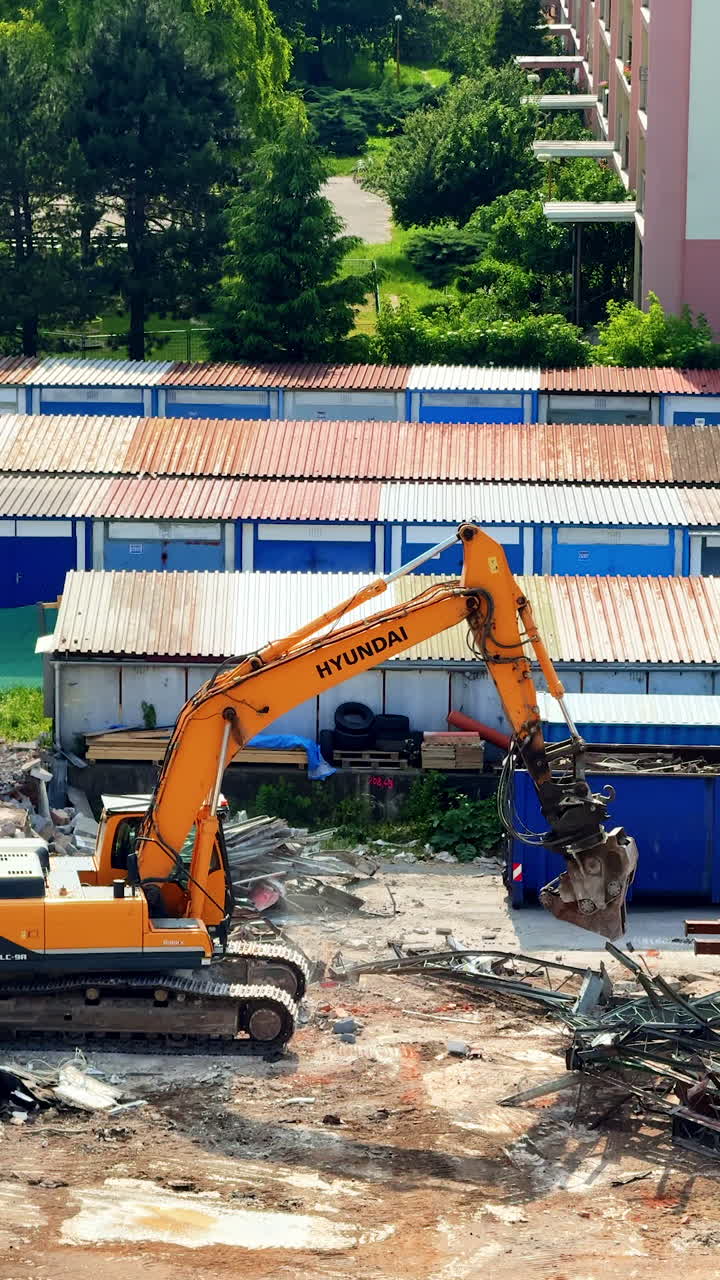 Machinery tears down old buildings. A large excavator works diligently at a demolition site, breaking down concrete and metal debris in an urban area
