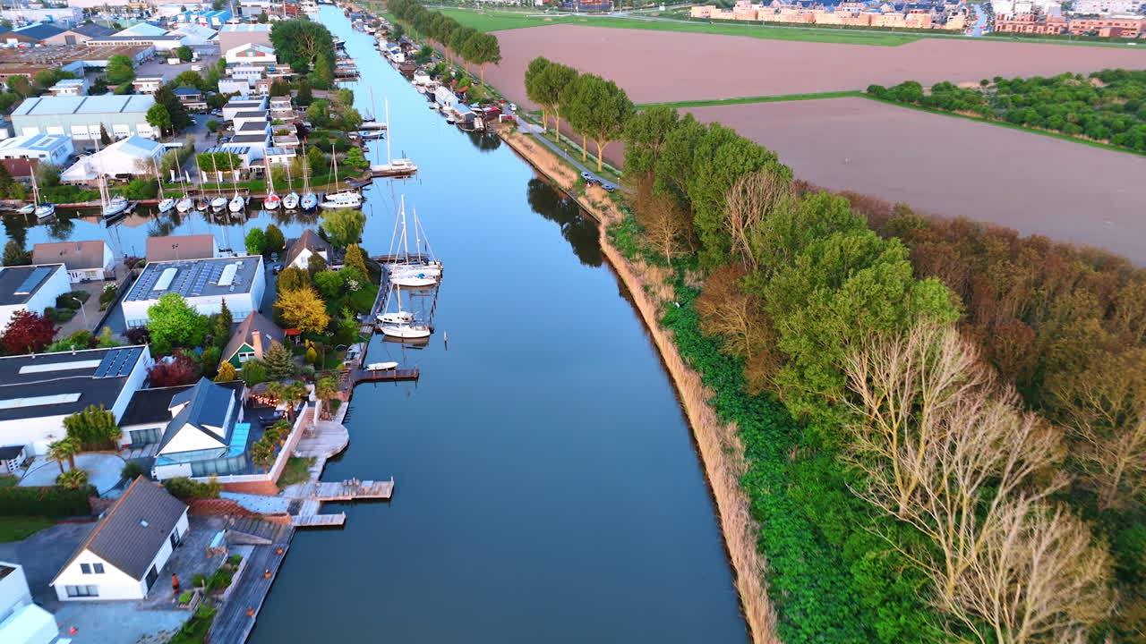 Flying over the mirror surface of the canal along the residential area. The Netherlands countryside at sunset time.