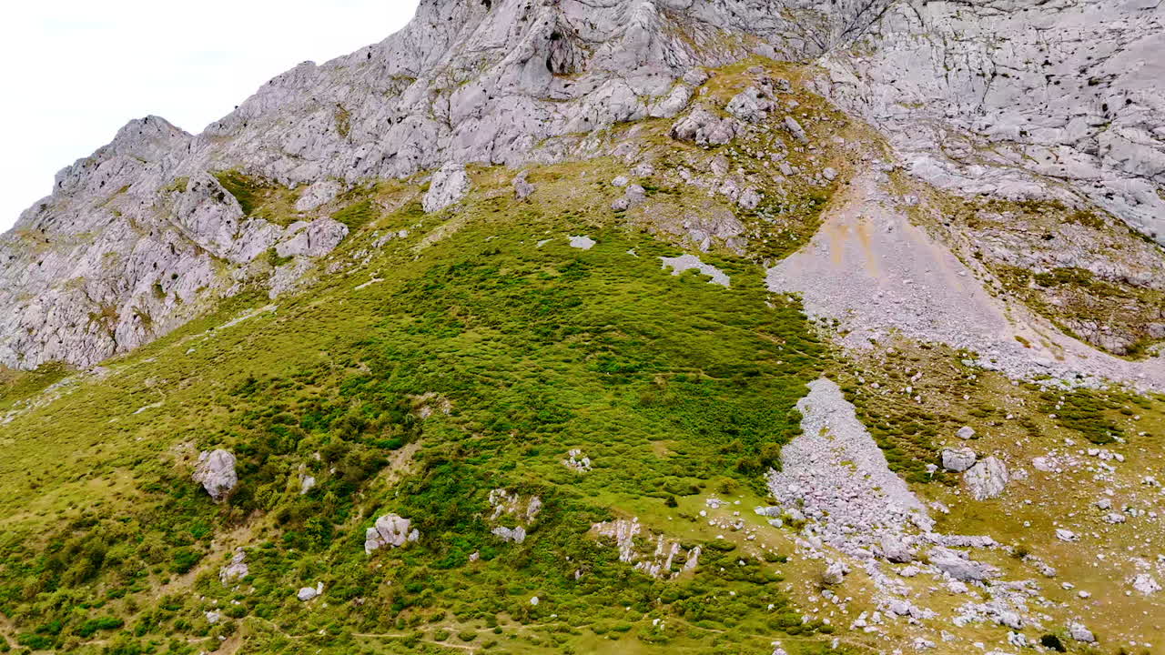 Rising along the green slope of the huge mountain covered with grass and lichens. Low angle view at grey top of the bare rock.