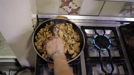 local pork cuisine preparation closeup clip on large black pan inside household kitchen, with someone's hand stirring it over.