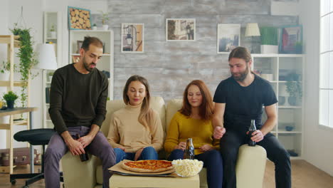 group of friends sitting on couch reaching out for pizza