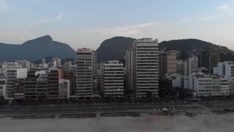 aerial backing off from empty ipanema beach early in the morning revealing the wider rio de janeiro cityscape with the corcovado mountain in the background at a hazy colourful sunrise
