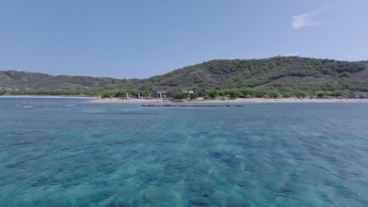 Ripresa aerea in avvicinamento del resort Puntarena a Baní, in una zona panoramica con verdi colline d'estate. Volo su acque cristalline nella Repubblica Dominicana.