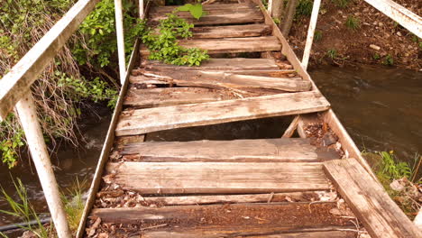puente de madera dañado sobre un pequeño río en el bosque