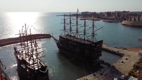 Fly-above-big-old-docked-wood-pirate-ship-in-sea-port-near-Avsallar-city