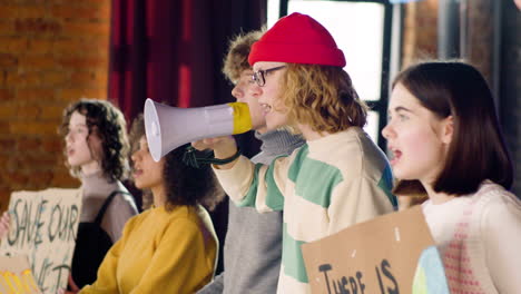 zijaanzicht van jonge milieuactivisten met borden en megafoon die protesteren tegen passiviteit door klimaatverandering