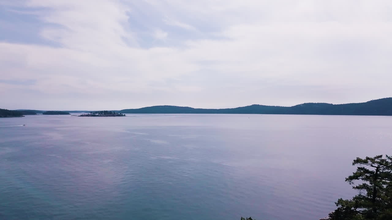 Drone lowering from horizon view over water to cover with trees in foreground at Jones Island Washington