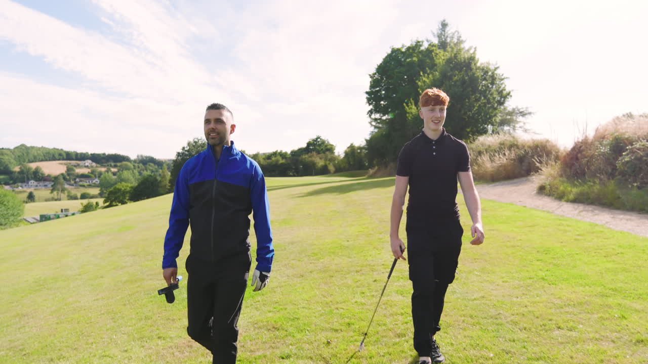 Two male golf players playing golf together, walking with clubs on a golf course on a sunny day