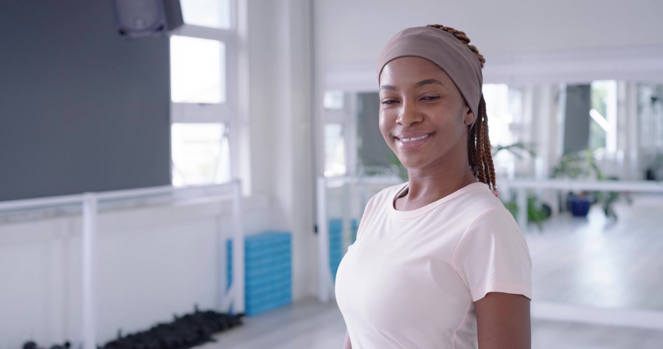 Femme africaine dévissant un bouchon de bouteille, buvant, respirant, se préparant près d'un miroir avec des haltères et des tapis