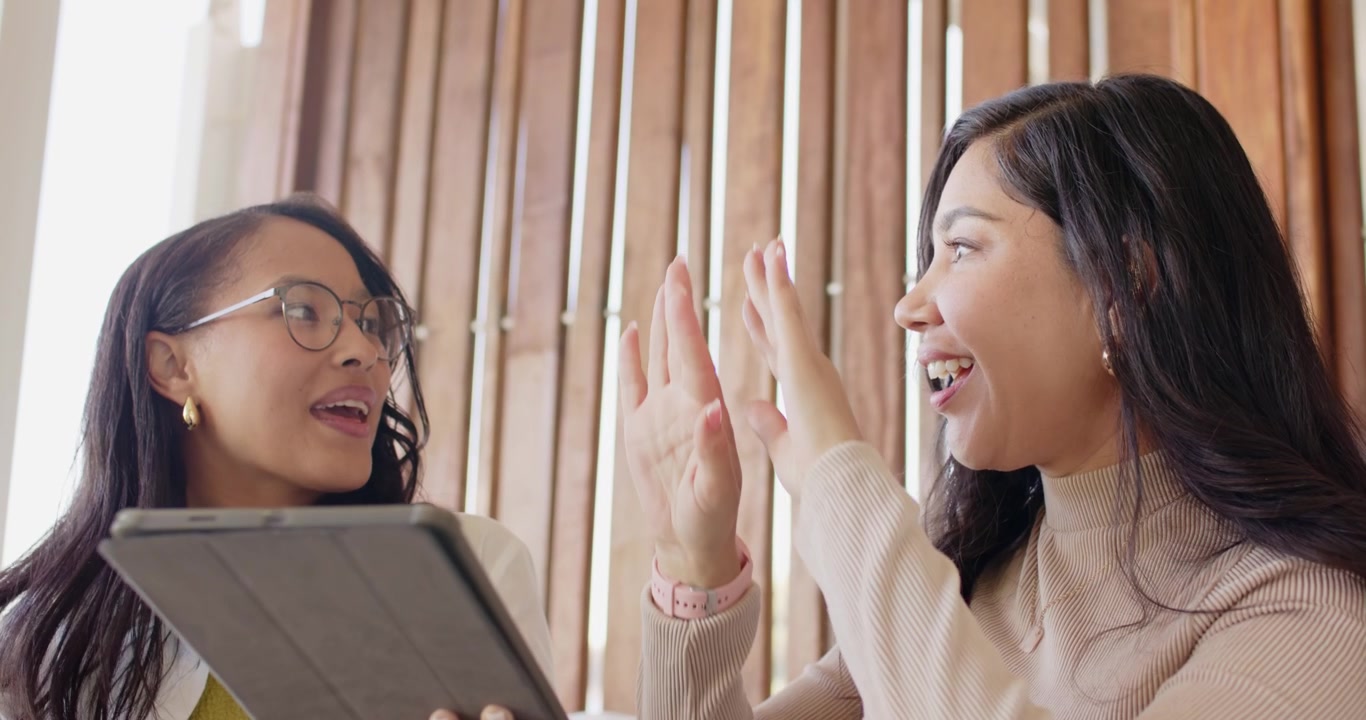 ソファに座った多様な女性の友人たちがタブレットを共有し、右側の女性がタップすると、二人とも驚きに反応する。