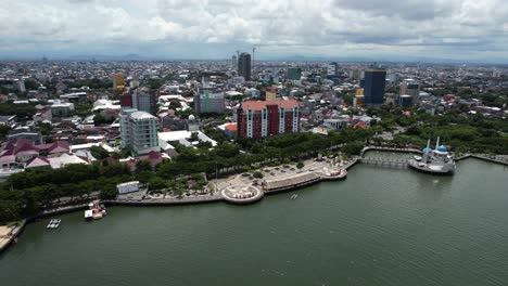 Vista-Aérea-De-La-Ciudad-De-Makassar-Sulawesi-Indonesia-En-Un-Día-Soleado-A-Lo-Largo-Del-Agua-Con-Una-Mezquita-En-La-Distancia