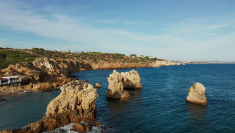 aerial orbiting shot of outstanding rocks on shoreline and private beach during sunny day at algarve,portugal