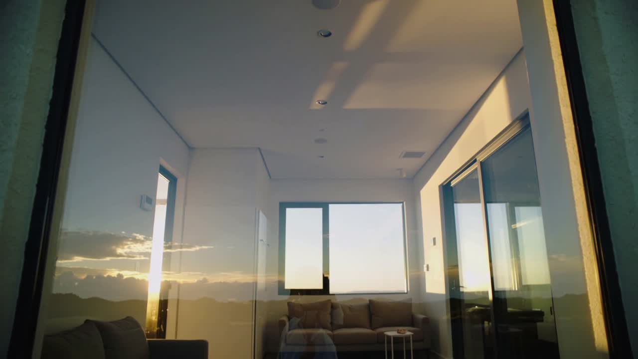 Telecamera che si inclina rivelando divano e tavolo del soggiorno attraverso il vetro, mostrando il tramonto e un leggero riflesso