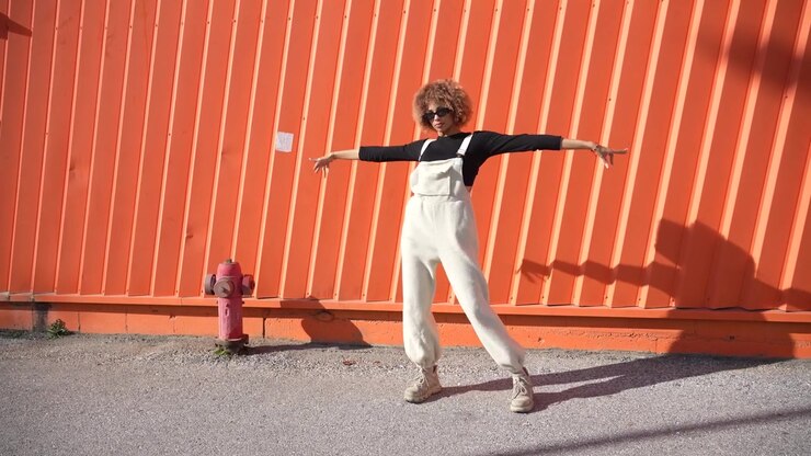 A fashionable and stylish young woman is posing gracefully against a vibrant orange wall
