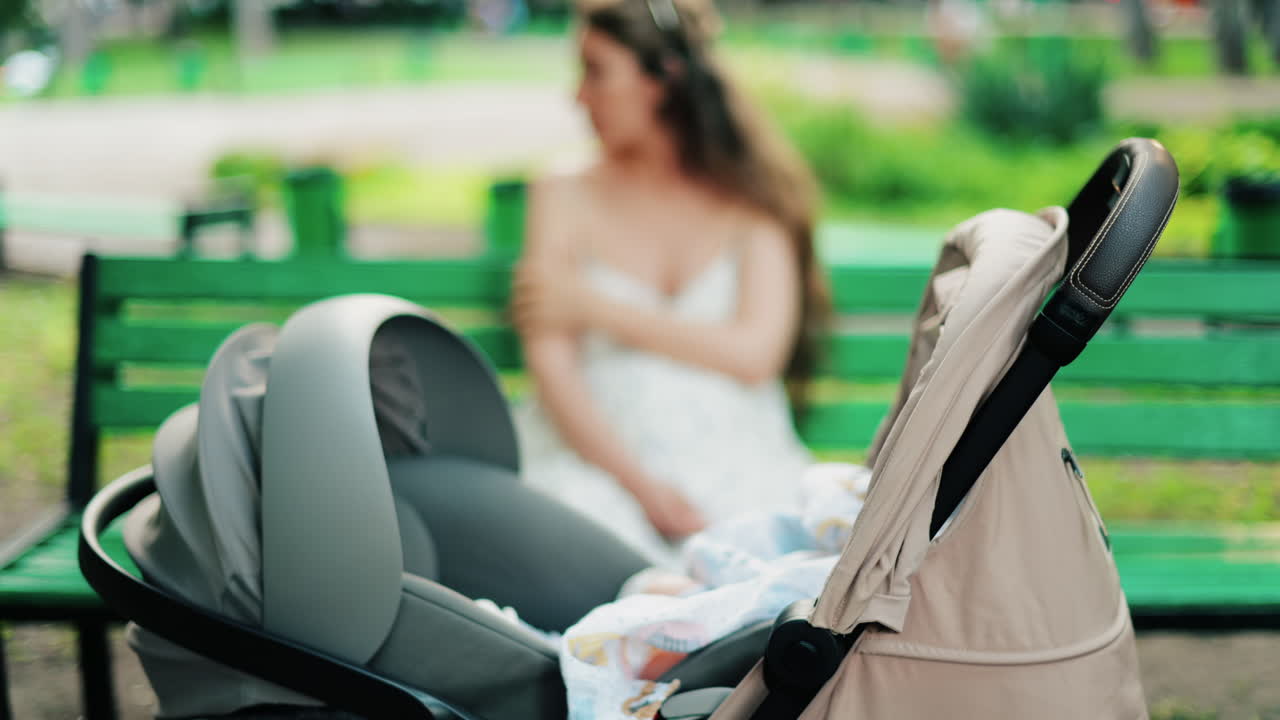 A baby resting in a stroller while a woman sits on a green bench in the background