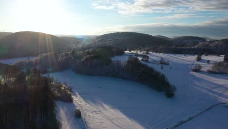 Stunning-aerial-panning-down-revealing-snow-covered-mountains,-forest-and-clear-sunny-sky-during-winter-in-Swabia,-Germany