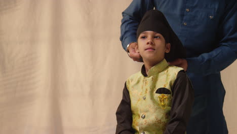 fotografía de estudio de un padre atando un turbante a la cabeza de un joven sikh que lleva un chaleco tradicional como secuencia parte 1 de 10