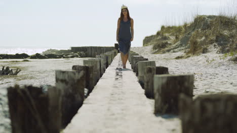 Female-Model-in-Sea-Shell-Crown-Walks-Toward-Camera-in-Slow-Motion-on-Wooden-Structure-at-the-Beach
