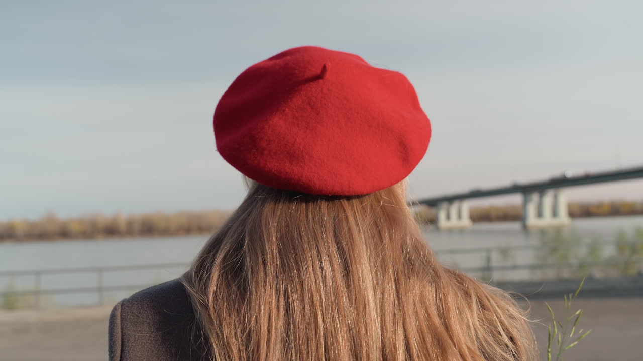 Donna vicino al fiume. Dolce giornata autunnale con una scena fluviale pacifica. Donna calma in piedi accanto al fiume con tempo ventilato. Donna tranquilla con berretto vicino al fiume in un ventoso pomeriggio autunnale.