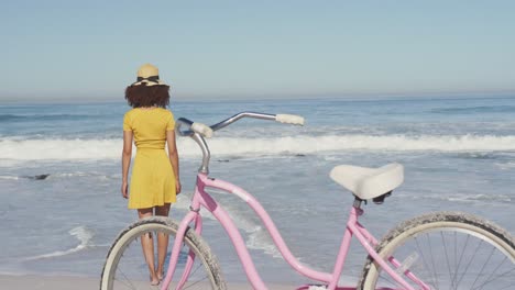 mujer afroamericana caminando por la costa con una bicicleta en primer plano