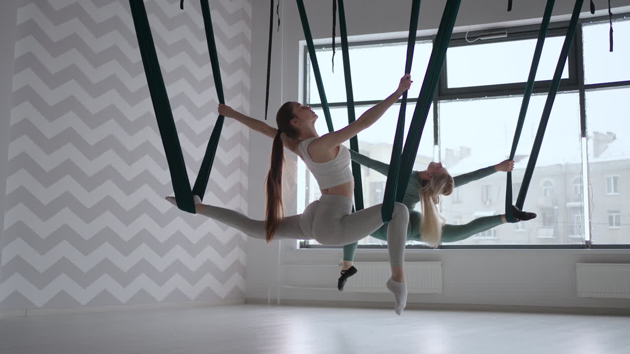 Two women perform twine on hammocks in the air. Stretch marks in the gym in the air. Aero Yoga