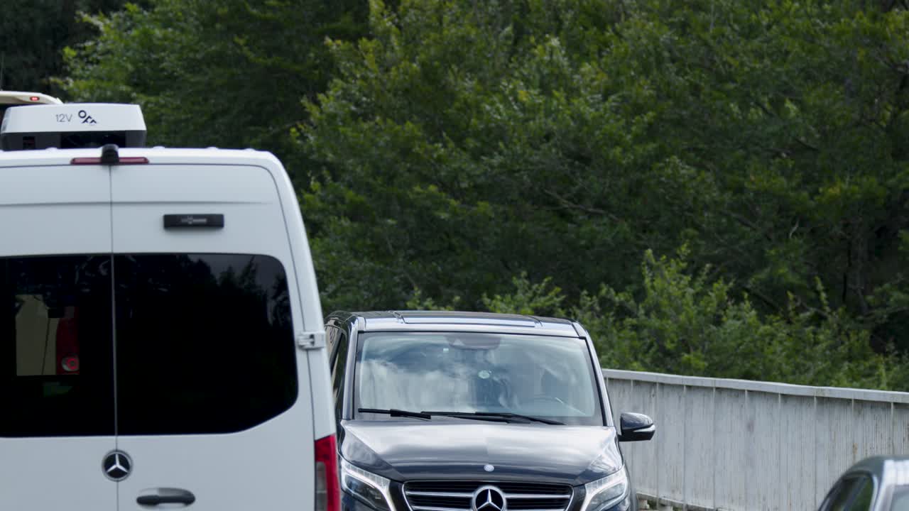 Multiple vehicles travel along a tree-lined road in the Scottish Highlands, demonstrating cooperation