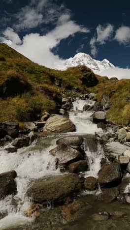 river waterfall stream and nepal mountains, vertical video for social media instagram reels and tiktok of beautiful flowing water river scenery and snowcapped himalayas mountain top landscape