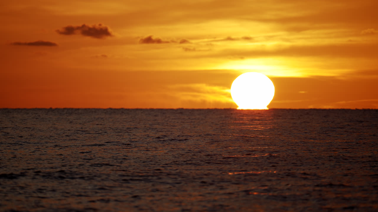Sun setting over Naples ocean, warm glow on horizon, tranquil coastal scene in Florida with ball of light illuminating warm sky