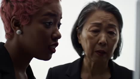 a thoughtful conversation between two women in professional attire, illuminated by soft light, reflecting a moment of understanding amidst a modern backdrop