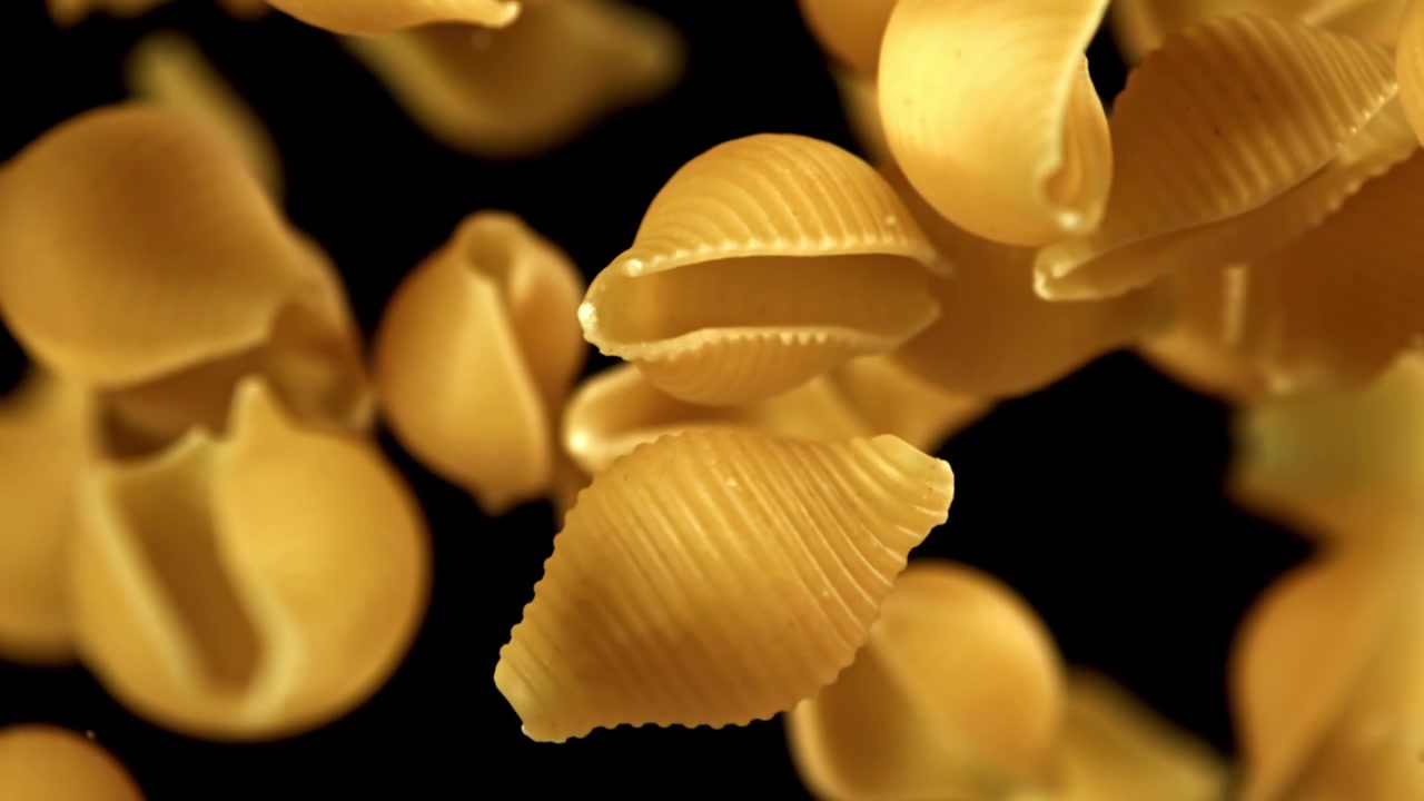 Rallentatore di pasta conchiglie secca che cade su sfondo nero
