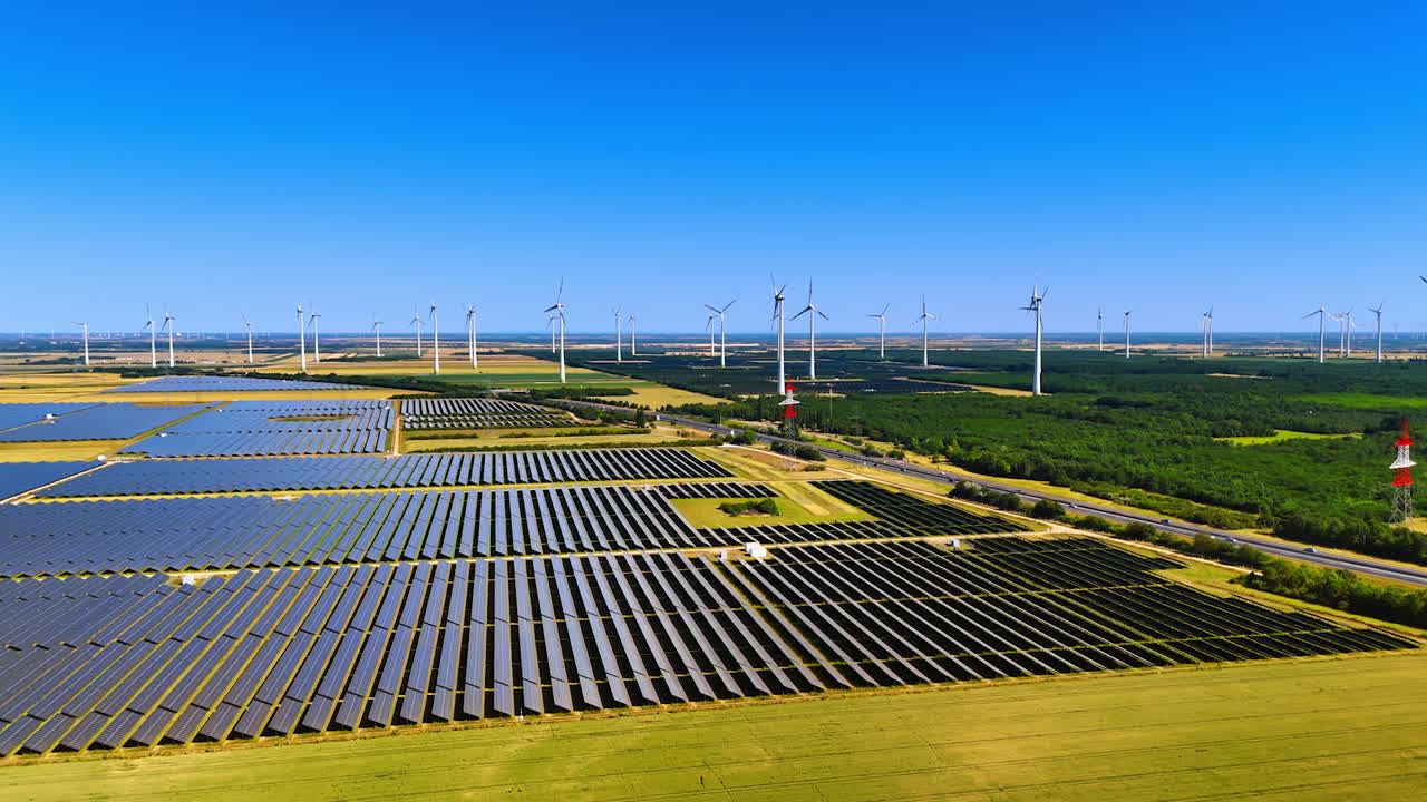Vast solar panels fields producing energy from sunlight. Wind farms make green energy from wind. Alternative power production. Aerial view