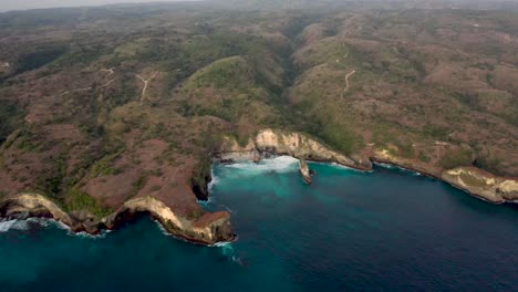 Vista-Aérea-De-Las-Olas-Del-Océano-Turquesa-Rompiendo-La-Costa-De-La-Playa-Rota-Famoso-Lugar-Turístico-En-La-Isla-De-Nusa-Penida,-Indonesia