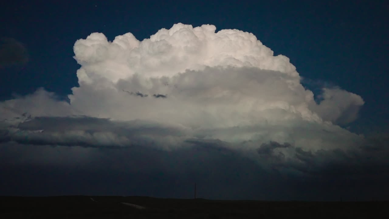 Glowing clouds lit by lightning during torrential rain over vast rural landscape