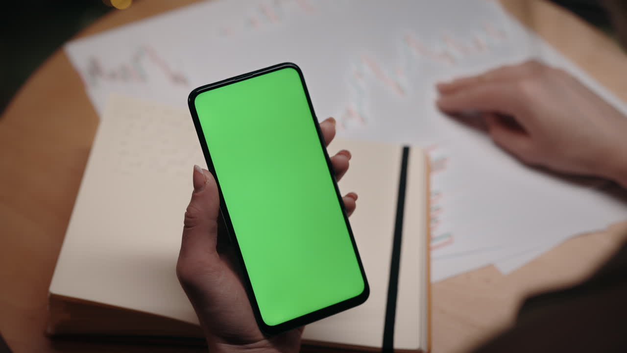 Smartphone con schermo verde su scrivania con grafico del mercato azionario