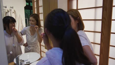 Asian-mother-and-daughter-standing-in-bathroom-and-brushing-teeth