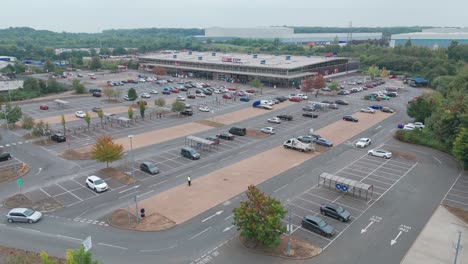 aerial view of a parking lot with multiple cars and a large building in the background under an overcast sky, showcasing organized infrastructure and surrounding greenery