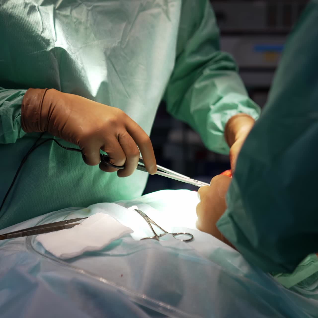 Uniformed surgeon in beige latex gloves uses electric device at operation. Metal tools and band are on the patient at doctor's approachability