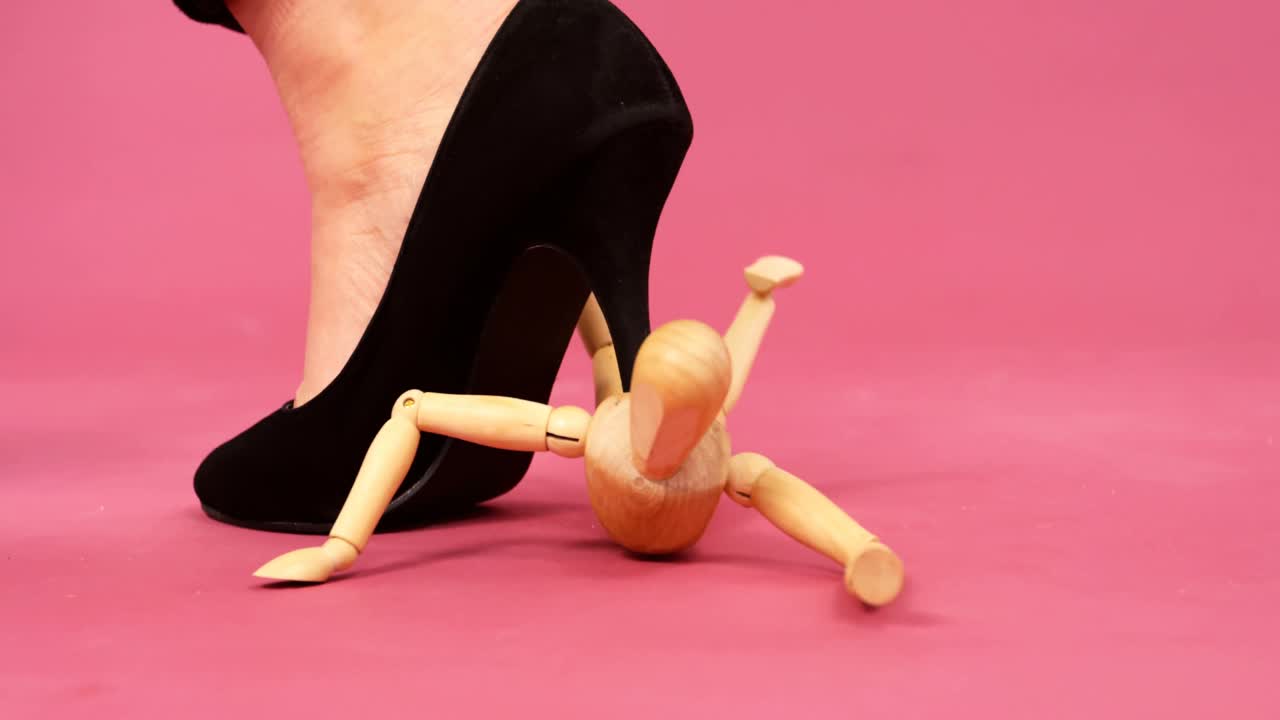 Frauenfuß mit schwarzem Stiletto zertritt eine Figur