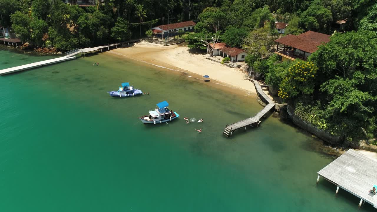 clip de vuelo de drones de un pequeño resort de playa de lujo en paraty rio de janeiro brasil con botes y gente nadando, agua turquesa y paz